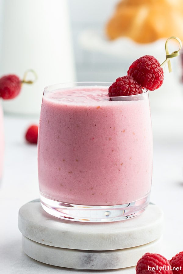 straight on picture of raspberry lassi in glass tumbler with fresh raspberries on toothpick