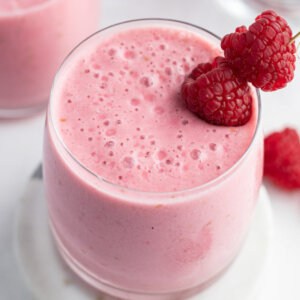 raspberry lassi in glass with fresh raspberries as garnish