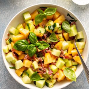 overhead Melon Cucumber Salad in white serving bowl with fresh basil leaves