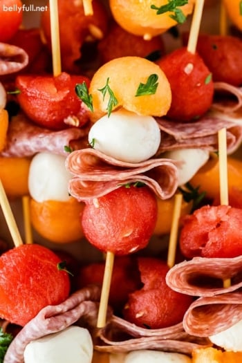 close up of mini fruit kabobs including watermelon, cantaloupe, fresh mozzarella, and salami,