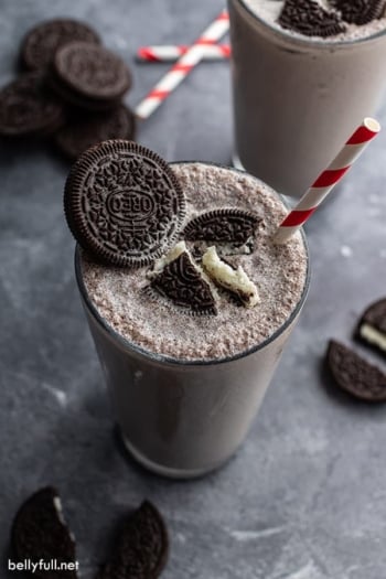 Oreo milkshake in soda fountain glass with crushed oreos and a red and white striped straw