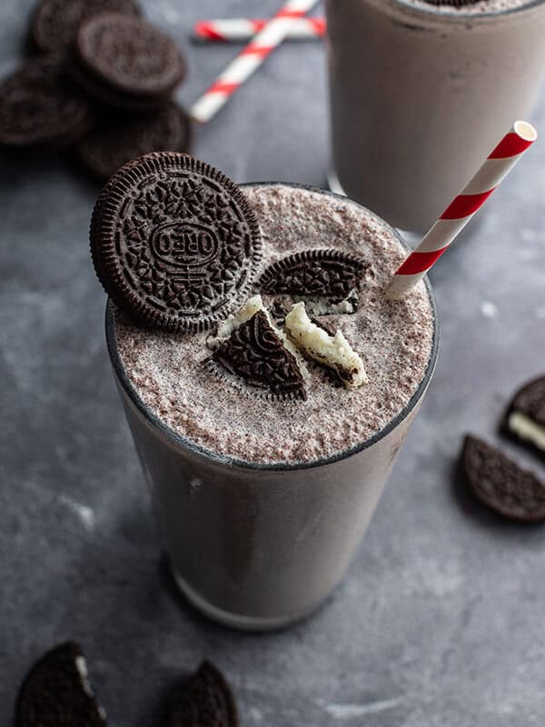 Oreo milkshake in soda fountain glass with crushed oreos and a red and white striped straw