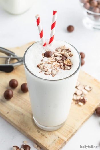 vanilla malted milkshake in a tall glass with crushed up malted milk balls and a red white striped straw