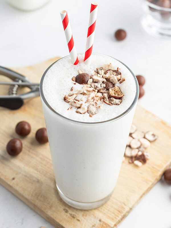 vanilla malted milkshake in a tall glass with crushed up malted milk balls and a red white striped straw