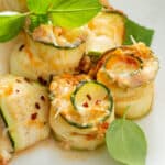 close up picture of baked zucchini lasagna rolls on white plate with basil leaves