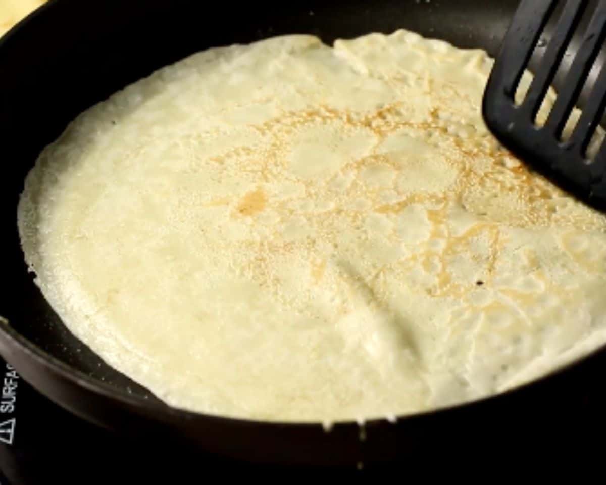 Loosening the edges of a cooked blini with a spatula before flipping