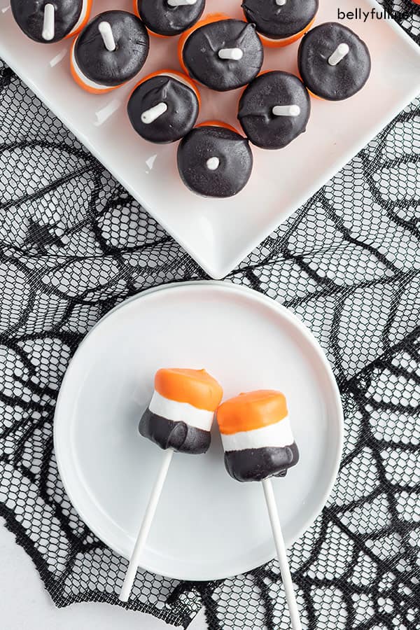 overhead of 2 Halloween Marshmallow Pops on white plate on top of black spiderweb tablecloth