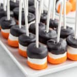 white tray of of black and orange candy coated marshmallows on a stick