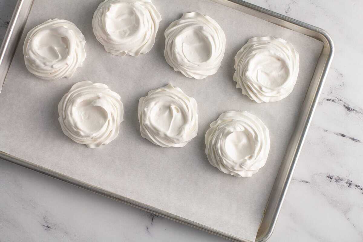 Mini pavlovas on a baking sheet with an indent on top.
