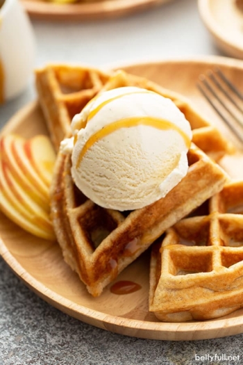 close up of apple waffles on brown plate with a scoop of vanilla ice cream and caramel drizzle