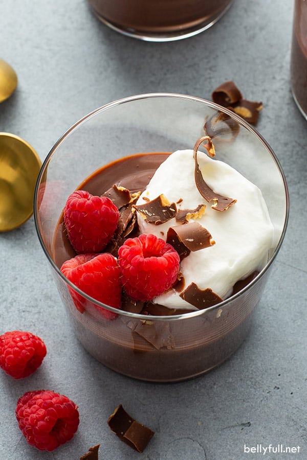 overhead glass of homemade pudding with whipped cream, chocolate shavings, and fresh raspberries