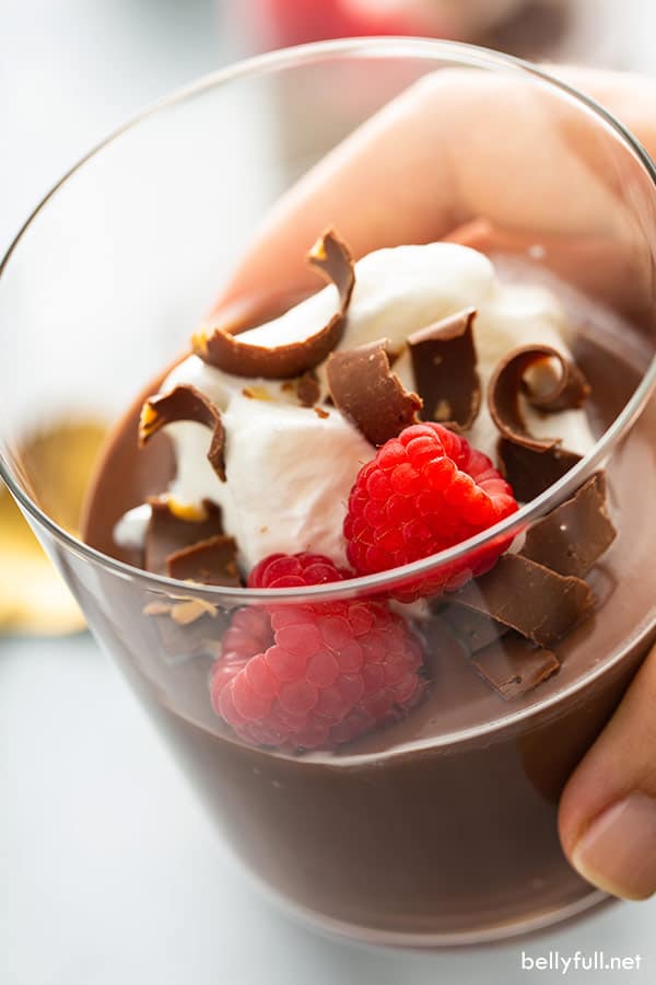 hand holding a glass with pudding and raspberries