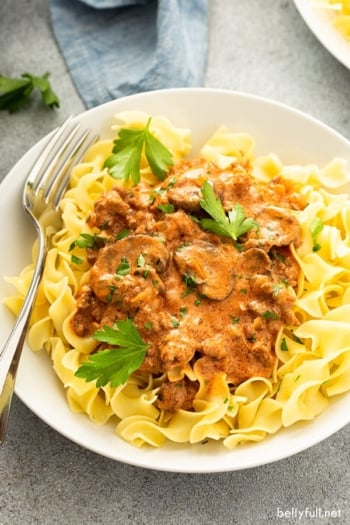 creamy beef and mushroom stroganoff sauce over cooked egg noodles in white bowl