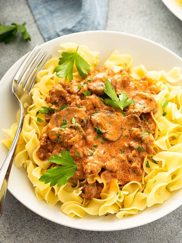 creamy beef and mushroom stroganoff sauce over cooked egg noodles in white bowl