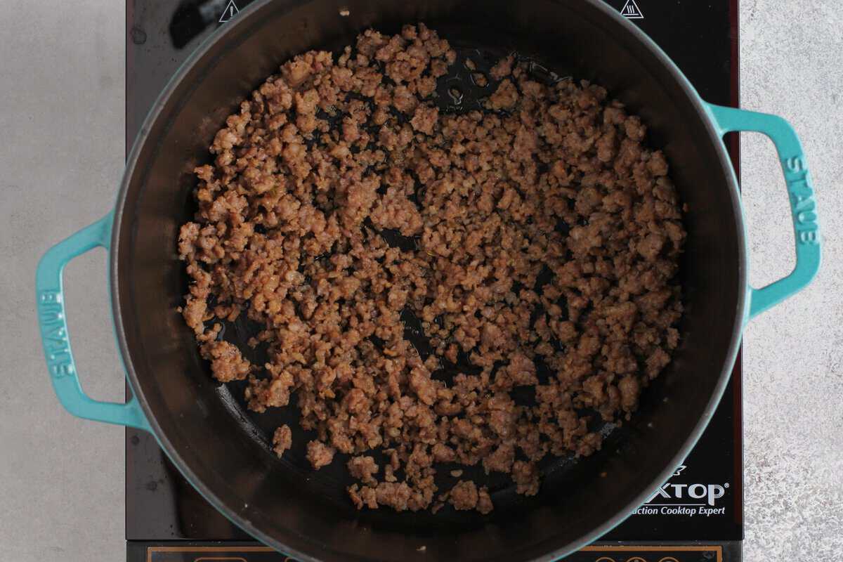 Cooking ground sausage in a Dutch oven with blue handles.