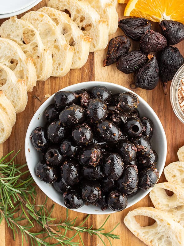 overhead of marinated black olives in white dish surrounded by crostini