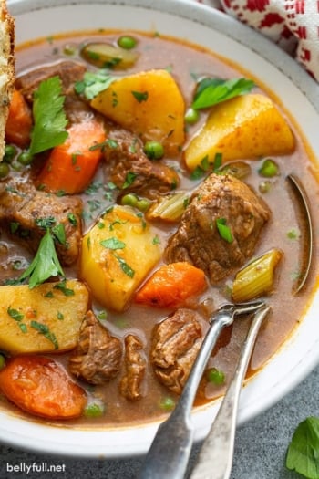 close up of beef stew in bowl with fork and spoon