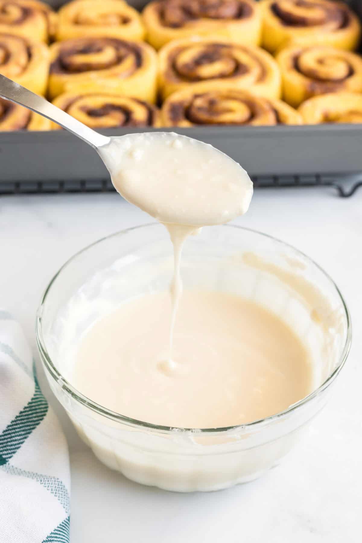 The frosting in a glass bowl with a spoon with frosting dripping over it.