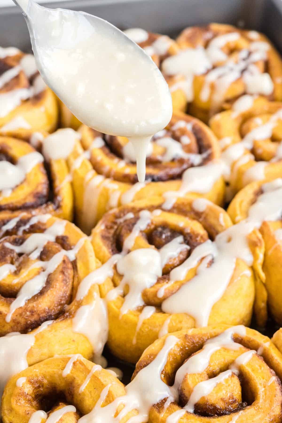 Drizzling the icing over the pumpkin cinnamon rolls.