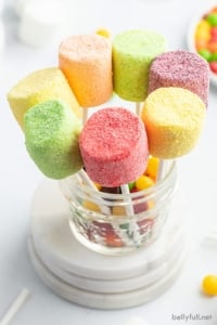 pink, green, yellow, and purple marshmallow pops standing in glass dish