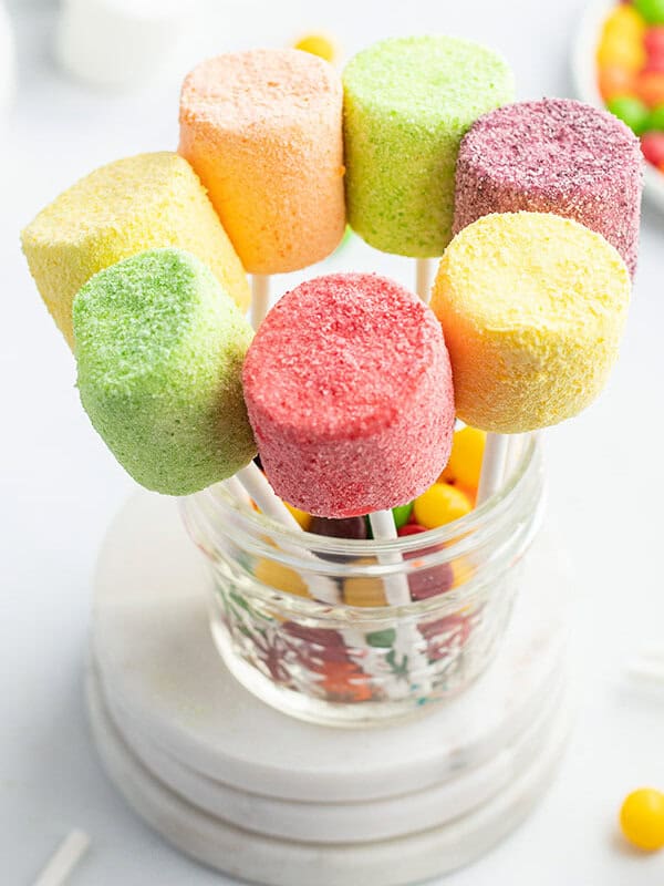 pink, green, yellow, and purple marshmallow pops standing in glass dish