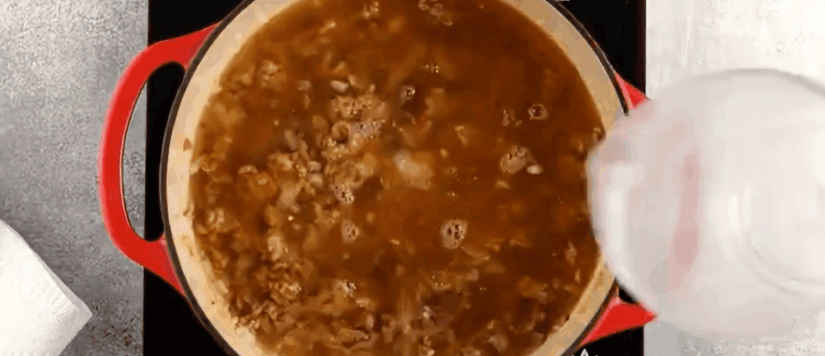Adding chicken stock to the pot with the pork. 