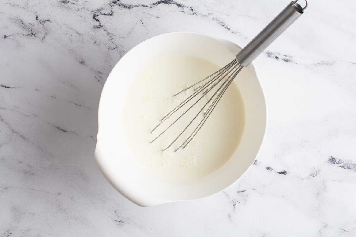 Combining the whole milk and heavy cream in a white bowl with a whisk.