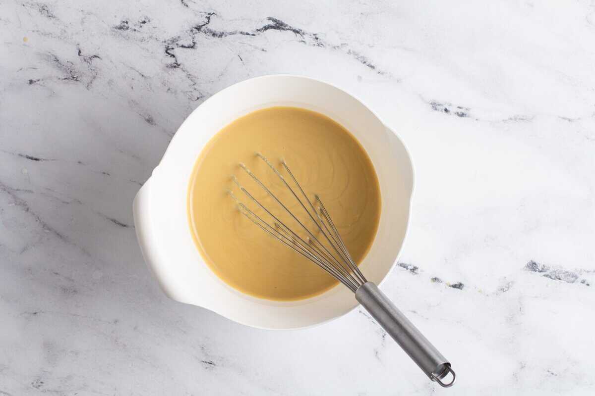 Tempering the eggs with the butterscotch mixture in a white bowl with a whisk.