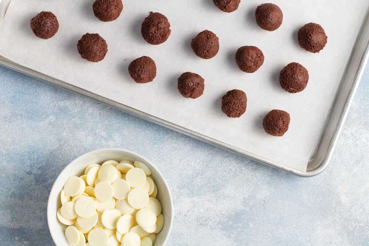 Chocolate truffles on a lined baking sheet with a bowl of candy melts.