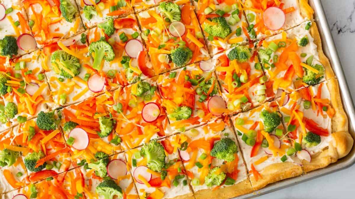 Pizza dough with cheese and veggies scattered on top.