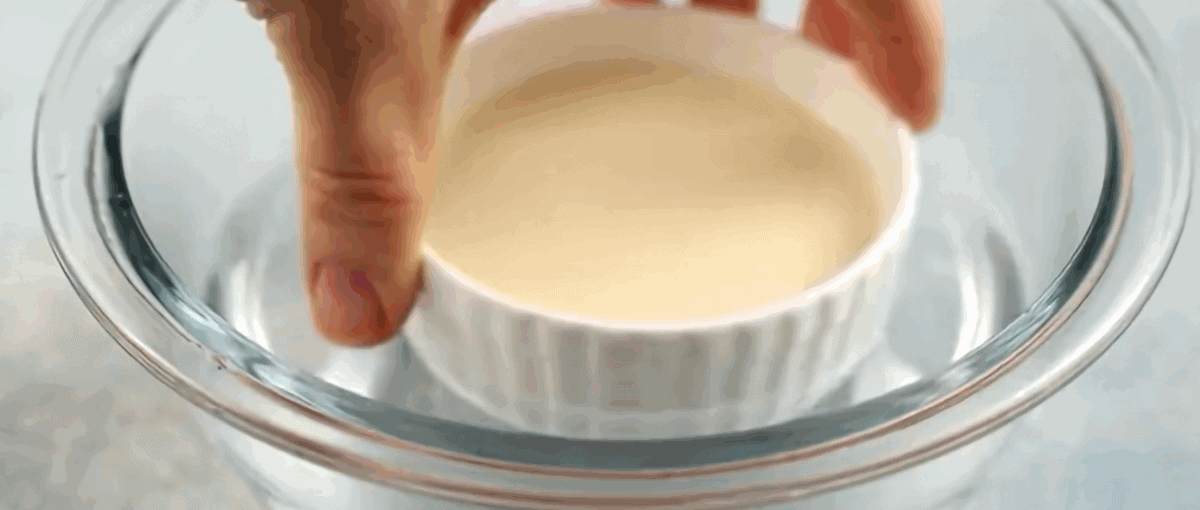 Dipping a ramekin into a bowl of hot water.