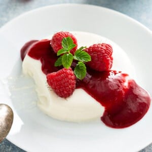 panna cotta unmolded onto white plate with raspberry sauce
