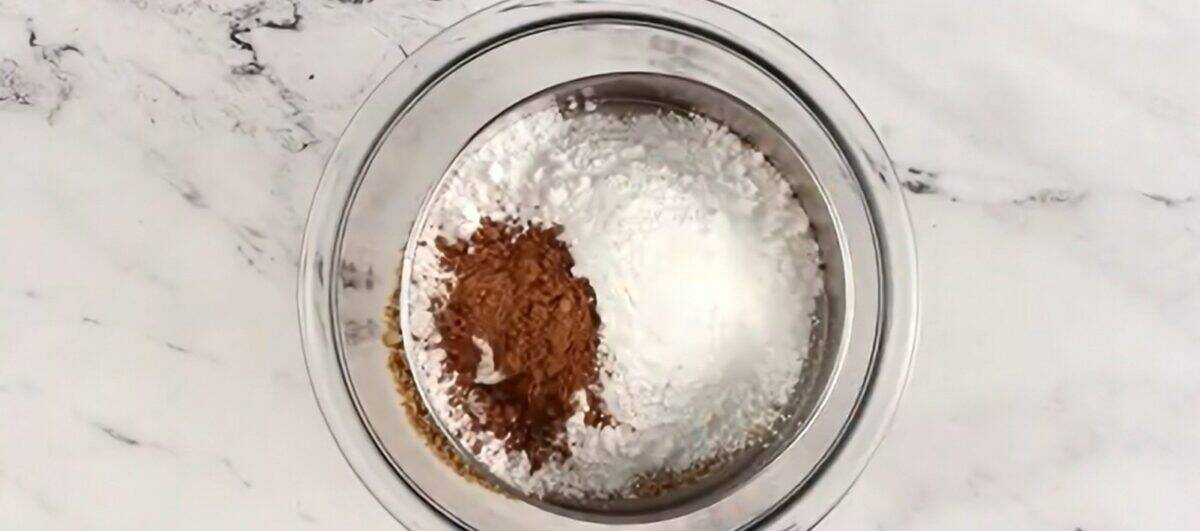 Sifting the dry ingredients into the bowl of cookie and pecan crumbs.
