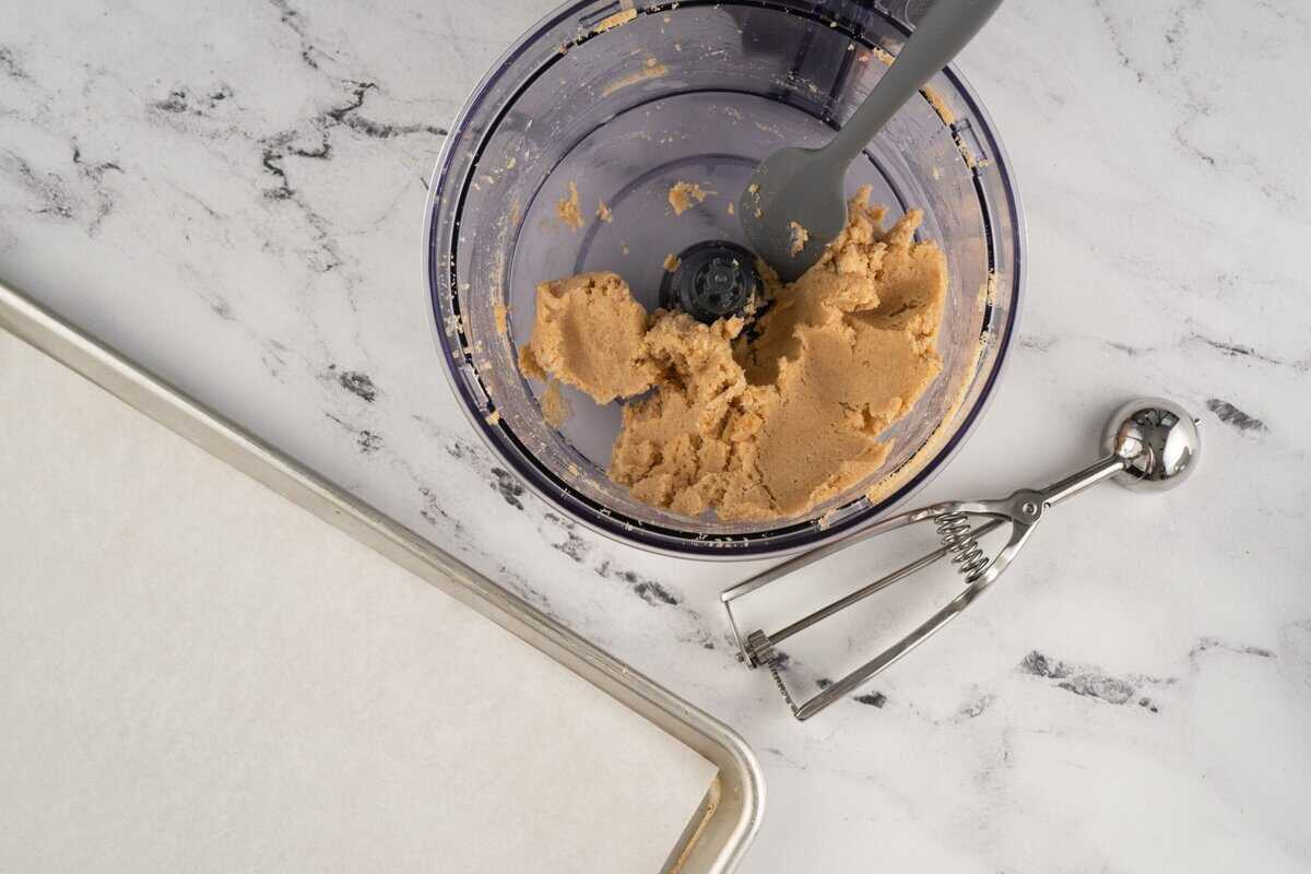 Sugar cookie truffle dough in a food processor with a cookie scoop next to it.