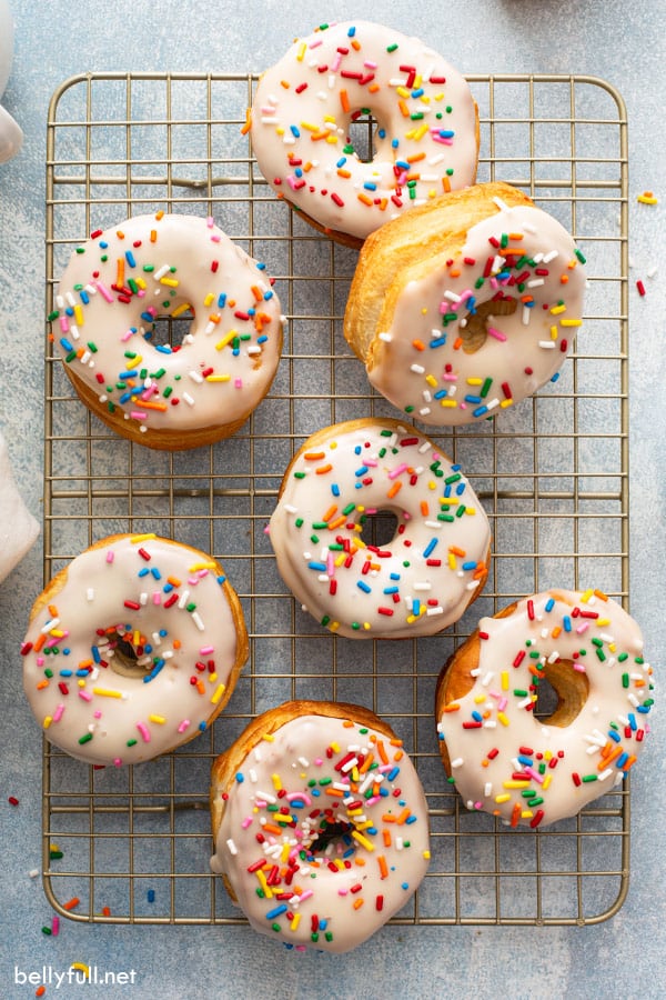 overhead of 7 donuts on cooling rack with glaze and sprinkles