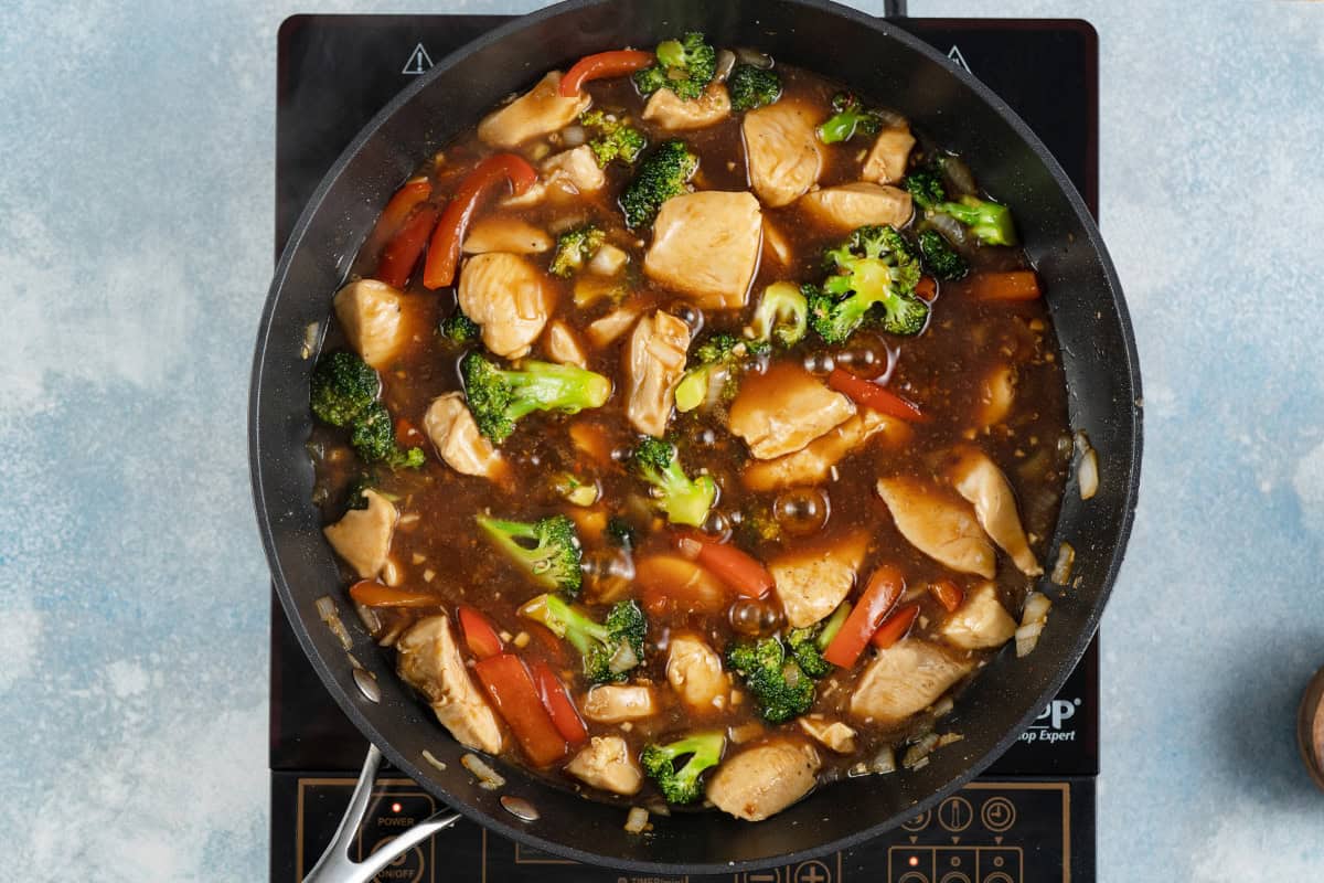 Chicken and veggies in the sauce in a skillet.