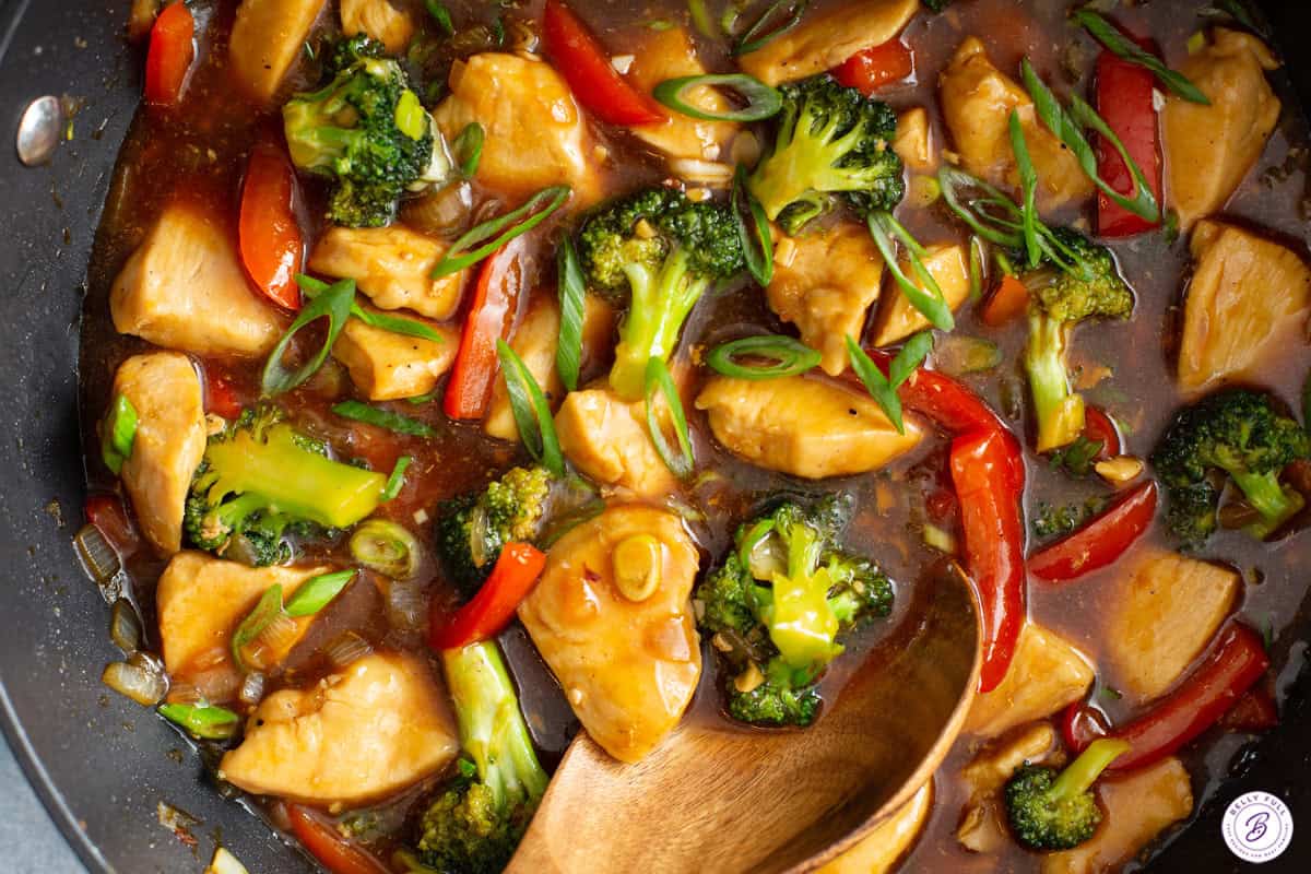 Chicken stir fry being stirred with a wooden spoon.