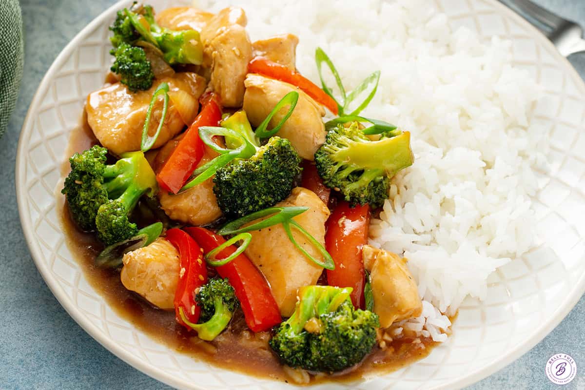 Chicken stir fry with white rice on a white plate.