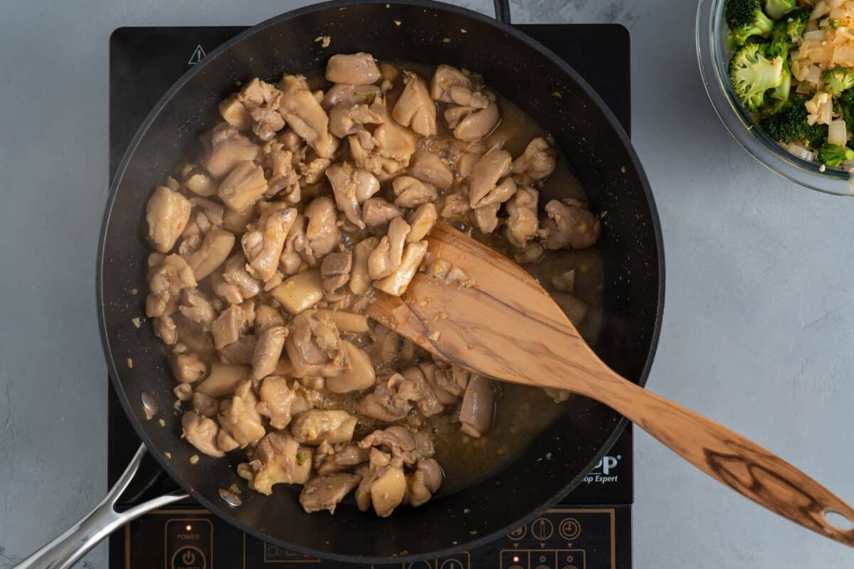 Cooking the chicken in a skillet with a wooden spoon.