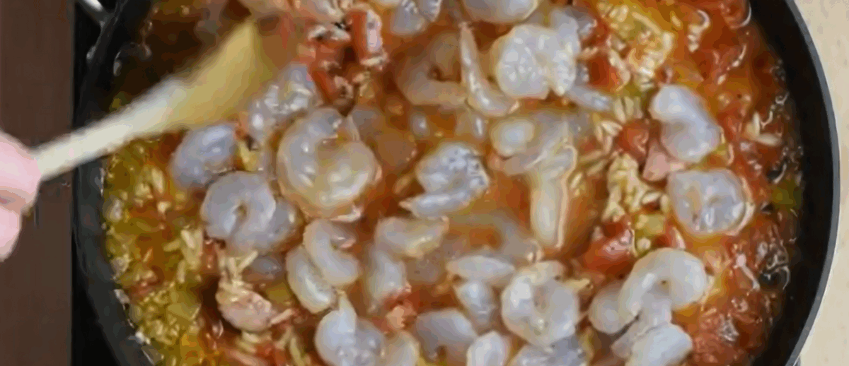 Adding shrimp to the pot with the other jambalaya ingredients. 