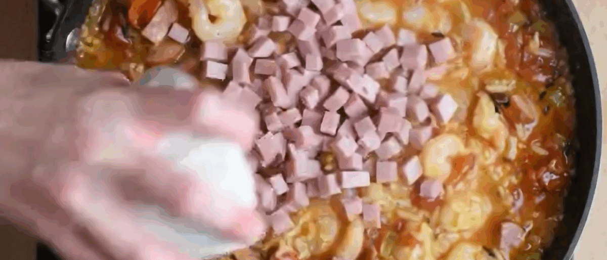 Adding cubed ham to the pot with the other jambalaya ingredients.