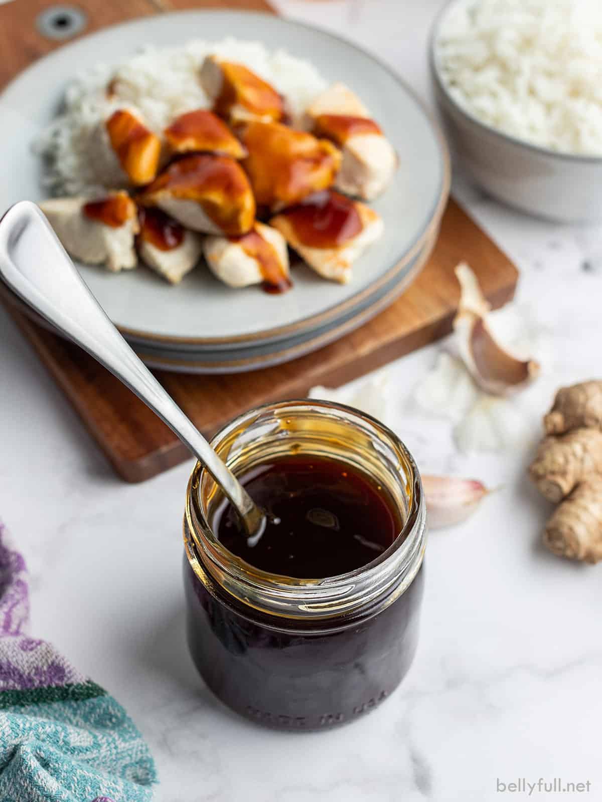 Jar of teriyaki sauce with chicken in the background.