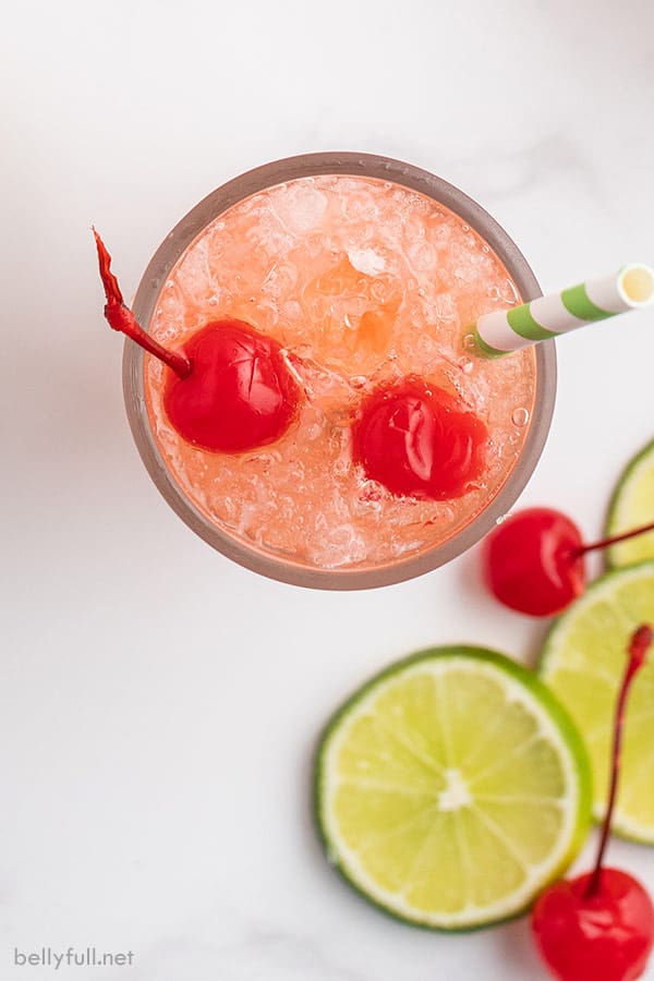 overhead shot of fizzy drink garnished with maraschino cherries and striped straw