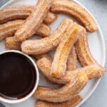 top down Churros on white plate with cup of chocolate sauce