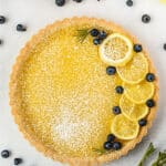 whole lemon tart garnished with lemon slices, blueberries, and powdered sugar