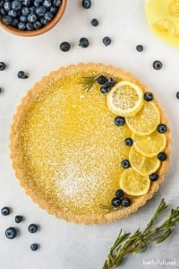 whole lemon tart garnished with lemon slices, blueberries, and powdered sugar