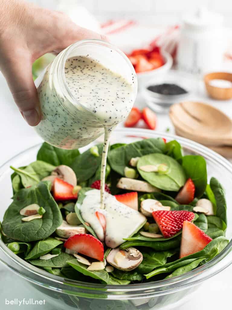 poppy seed dressing being poured over salad