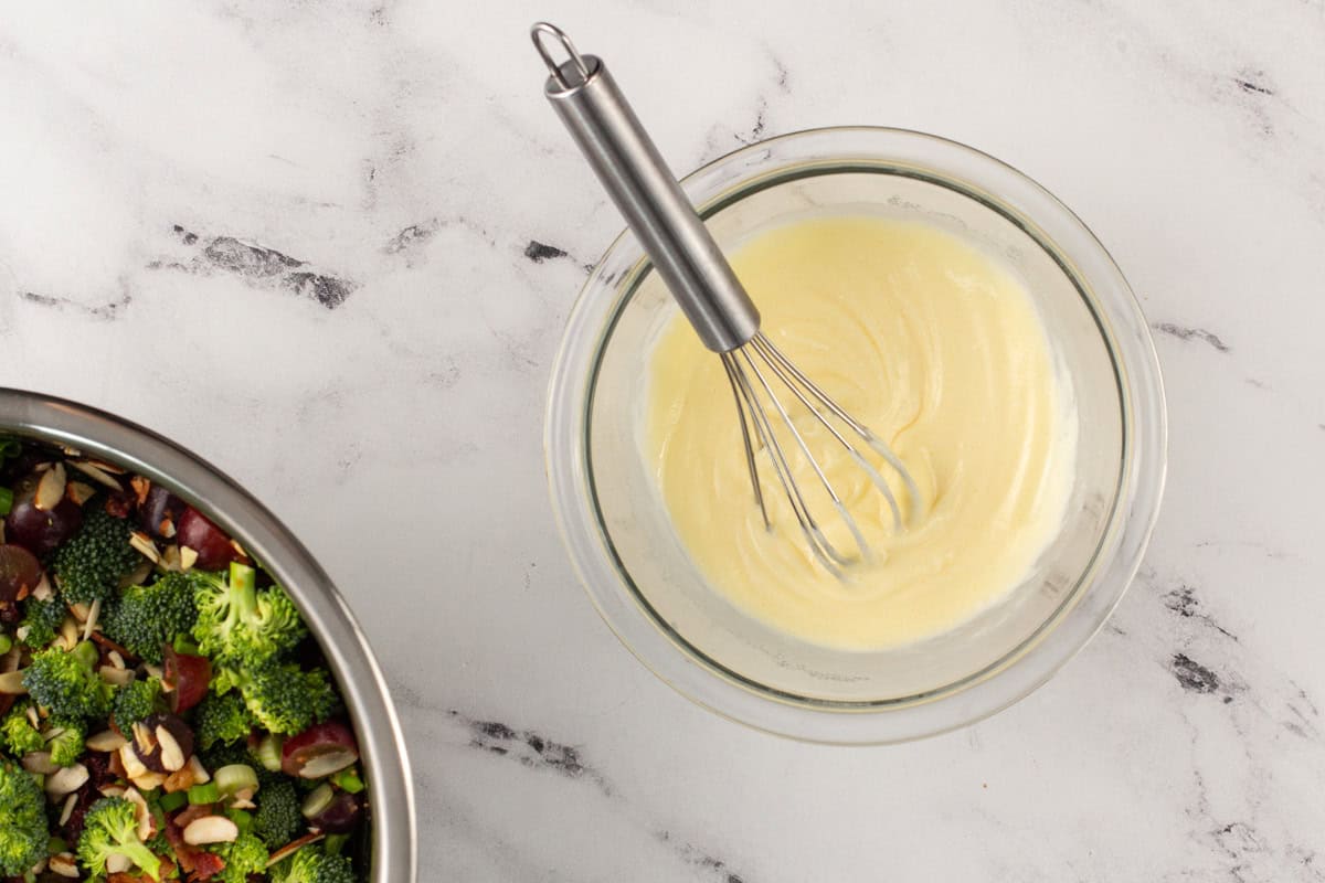 Dressing for broccoli salad in a bowl with a whisk.