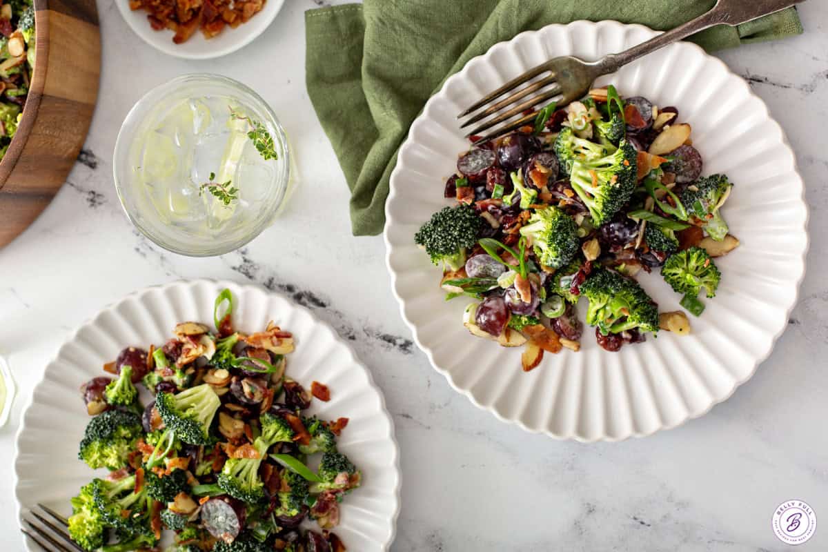 2 plates of broccoli salad with a fork on one plate and an empty glass bowl.