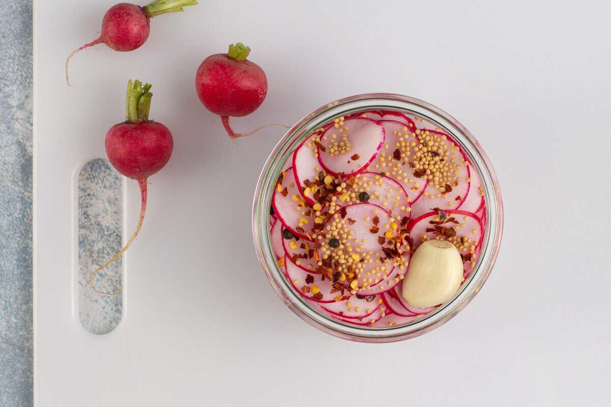 Sliced radishes in a jar with pickling spices.